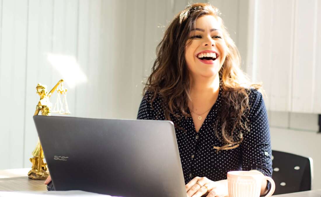 A female entrepreneur or small business owner working at a laptop in a sunny office with a satisfied smile on her face