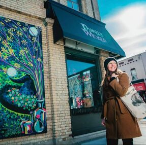 A female shopper bundled up for cold weather shopping in downtown St. Thomas in the sun. Pictured in front of The Magic of Nature mural and the awning of Purely Wicked.